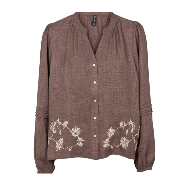 Harriet Blouse fra prepair er en elegant og feminin bluse med smukke broderede blomsterdetaljer langs kanten. Blusen har en lille V-udskæring og gennemgående knapper foran. De fine læg ved skuldrene og de dekorative læg på ærmerne giver et let og smukt udtryk. Ærmerne afsluttes med elastik for et blødt, puffet look.